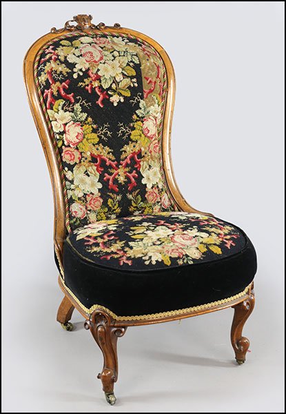 AN ENGLISH CARVED WALNUT SLIPPER CHAIR.: AN ENGLISH CARVED WALNUT SLIPPER CHAIR. Bearing needlepoint upholstery, a carved 'C' at the crest, and raised on casters Back H: 38.5''