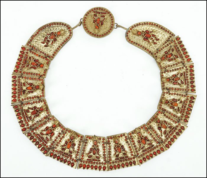A NEPALESE CORAL AND GILT METAL WEDDING NECKLACE.: A NEPALESE CORAL AND GILT METAL WEDDING NECKLACE. Comprising fifteen links of studded coral which form a seated figure wearing a headdress Length: 25"