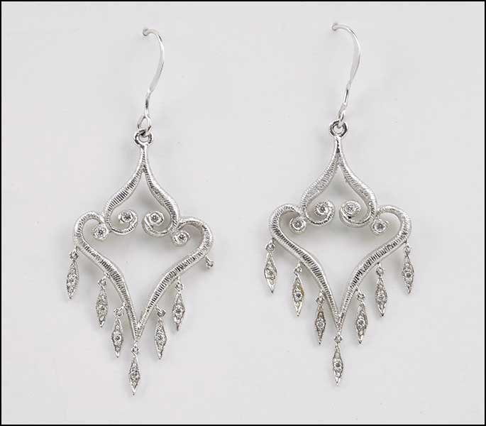 A PAIR OF PENNY PREVILLE DIAMOND AND PLATINUM DROP: A PAIR OF PENNY PREVILLE DIAMOND AND PLATINUM DROP EARRINGS. Each scroll form earring contains four bezel set round white diamonds towards the top and seven round white diamonds suspended from lower e