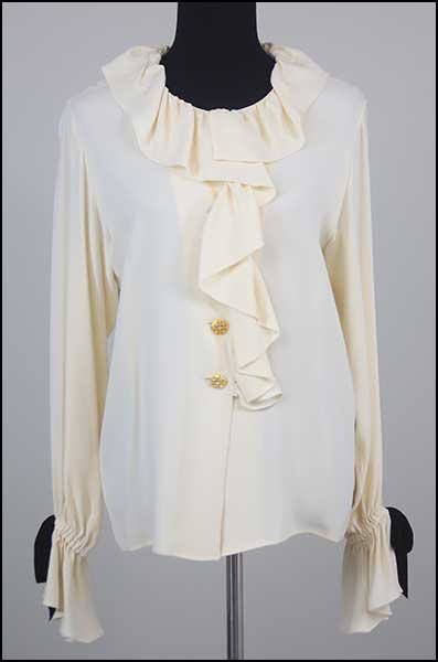 AN YVES SAINT LAURENT RIVE GAUCHE SILK BLOUSE.: AN YVES SAINT LAURENT RIVE GAUCHE SILK BLOUSE. Containing ruffles on collar and draped over goldtone buttons. Each sleeve contains a ruffle cuff with a black velvet bow Size: 40