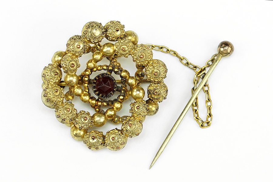 An Edwardian Garnet And Gold Filled Brooch.: An Edwardian Garnet And Gold Filled Brooch. Textured gold design contains one central round garnet. Bearing stick pin attachment Brooch: 1.25"