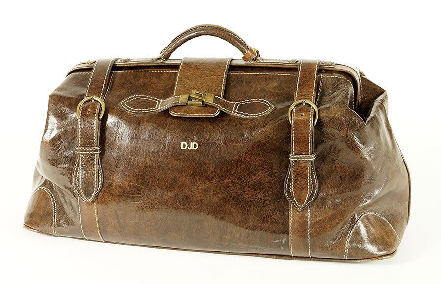 A Brown Leather Satchel Style Suitcase.: A Brown Leather Satchel Style Suitcase. With luggage tag. Bearing goldtone hardware and embossed monogram 'DJD' Approximate Size: 11" x 24" x 9"