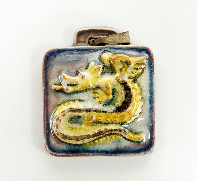 A Karlsruhe German Majolica Art Pottery Dragon Pendant.: A Karlsruhe German Majolica Art Pottery Dragon Pendant. Pendant depicts a repousse enamel dragon in browns and yellows against a blue enamel background. The back of pendant bears the mark "Karlsruhe".