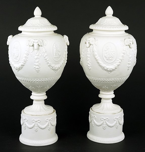 A Pair of Mottahedeh Parian Ware Urns.: A Pair of Mottahedeh Parian Ware Urns. Bearing floral garland swag and ram's head decoration to the perimeters, bearing maker's label on the underside Height: 16.5"
