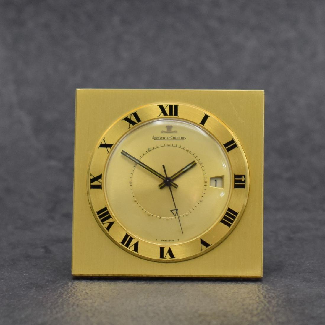 Jaeger-LeCoultre small table clock with alarm: Jaeger-LeCoultre small table clock with alarm, Switzerland around 1970, gold-plated case, snap on case back, bezel with Roman numerals, gilded dial, black hands, date, rhodium plated movement calibre