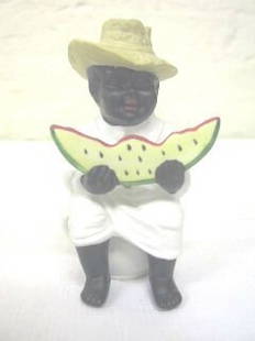 African American Seated Occupied Japan Figurine, Wa: This is a very cute seated figurine incised Occupied Japan. It is a young boy sitting on a pot. He is holding a slice of watermelon in both hands. There is a drilled hole in his left leg. He is 5"