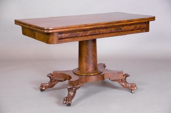 Classical carved mahogany dinning table. The hinge: Classical carved mahogany dinning table. The hinged rectangular top with rounded corners above a bolection apron and columnar pedestal on a shaped plinth on paw feet with leafy wings. THis empire dini