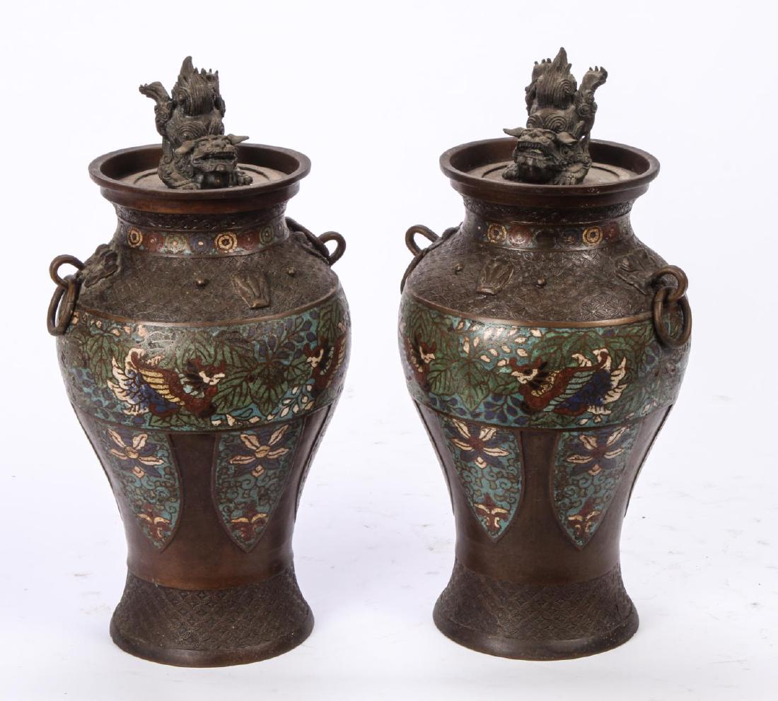 PAIR OF CHINESE BRONZE CHAMPLEVE URNS: Foo Dog finials, figural escutcheons for ring handles. Champlevé enamel band with birds and flora above lancet drops. 16 inches.