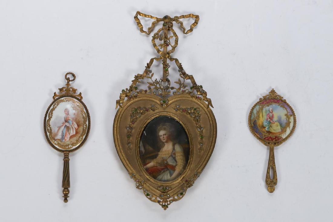 ELABORATELY FRAMED MIRRORS & PORTRAIT MINIATURE: (2) Small hand mirrors with beveled glass and porcelain backs hand painted with (18th c) costumed women. 5 1/2 and 4 1/2 inches. Unsigned portrait miniature is presented in a bejeweled heart shaped br