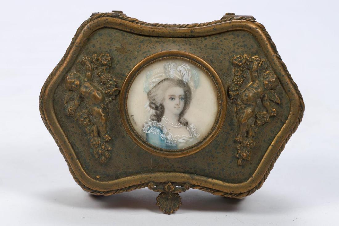 CONTINENTAL PORCELAIN BOX with BRONZE COVER: Set with hand painted portrait miniature flanked by cast bronze cherubs. Cover hinges open to reveal a conforming mirror. 1 1/2 x 3 3/4 x 3 inches.