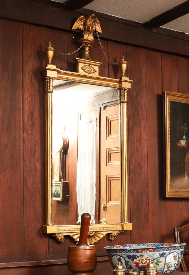 LARGE FEDERAL PERIOD GILT LOOKING GLASS: Patriotic eagle on plinth flanked by urns, split columns. Scrolled shell and bell flower drop. 51 x 22 inches.
