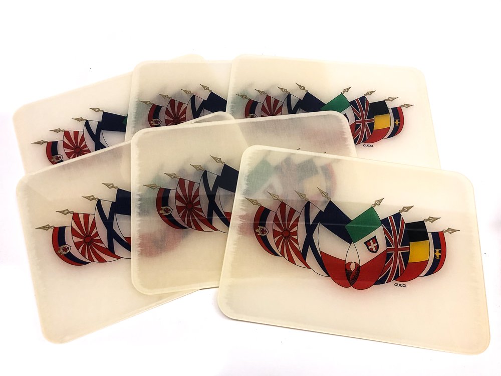 SET OF (6) VINTAGE GUCCI PLACEMATS W/ ORIGINAL BOX: Group of 6 vintage Gucci place mats. Mats have a linen core printed with flags of various nations. Reverse side has Gucci seal along with \"Gucci Made in Italy\".