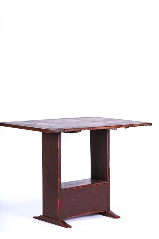 DIMINUTIVE TRESTLE TABLE IN RED PAINT: Worn top with breadboard ends, boxed stretcher with lid which opens to cabinet and shoe feet. 27 x 37 x 25 inches.