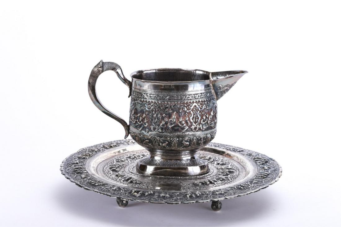 FAR EAST INDIAN SILVER PITCHER and FOOTED TRAY: Repousse (2) piece set with bands of figures seated around tables and in and out of doors all beneath a canopy of scrolls and flora. A second band has fish, goats, cows, elephant and scorpion. 8 x 13