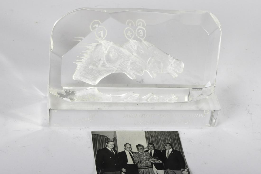 U.S.H.W.A. HUGH GRANT "GOOD GUY" AWARD: To Dorothy Haughton (First Lady of Harness Racing) intaglio cut acrylic sculpture by Michael Cox. 7 x 11 x 4 1/4 inches. Together with a photo of Dotty receiving the award.