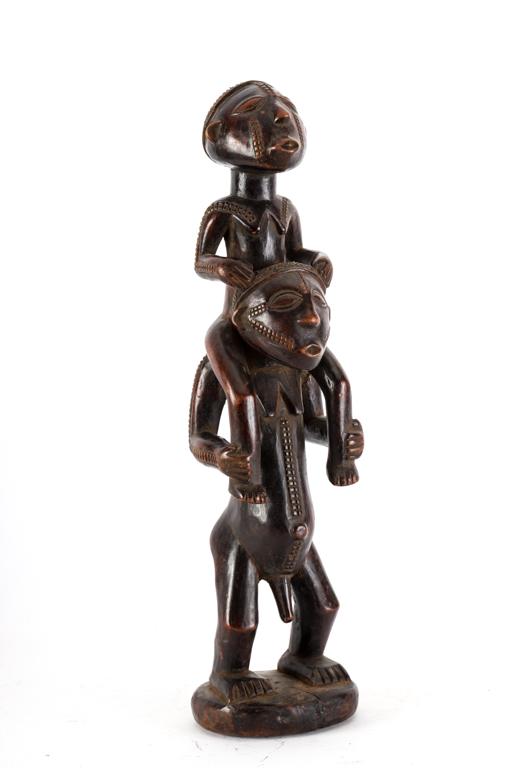 (2) WELL CARVED AFRICAN WOOD SCULPTURES OF MEN: Probably Mboko tribe (1) Holding an ostrich egg and a long reed pole and (1) Of a man with a boy on his shoulders. Each with body scarification, of good age and patina. 19 1/4 inches (and under)