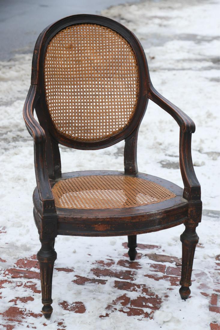 LOUIS XVI CANE-BACK ARMCHAIR: Molded oval back and arms terminating with scrolls, carved and molded cane seat raised on turned and fluted legs together with an upholstered cushion. 37 x 22 x 23 inches