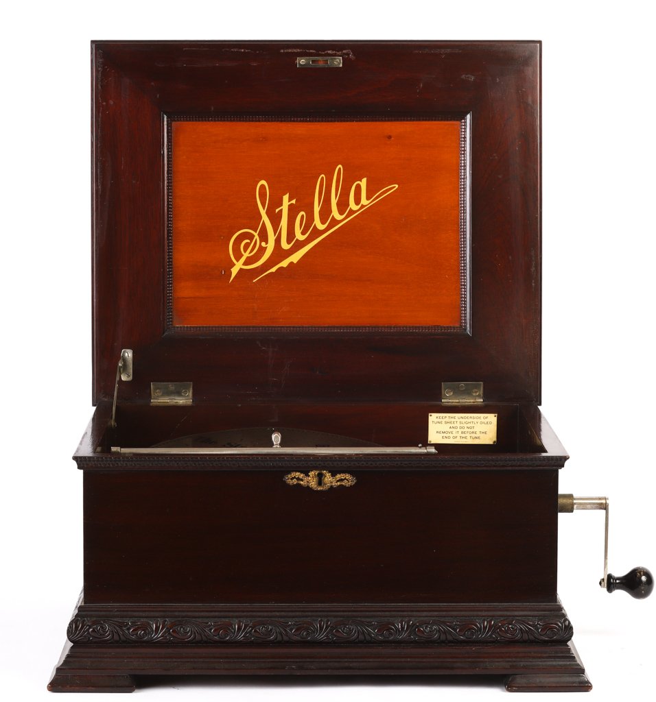 STELLA TABLE-TOP DISK MUSIC BOX c1897: Swiss made with mahogany case with Dutch ripple and scrolled molding raised on a molded base with offset feet. 11 x 24 x 19 1/2 inches. Retailed by Hermann A. Ockel, Providence, RI. Together with 0ver