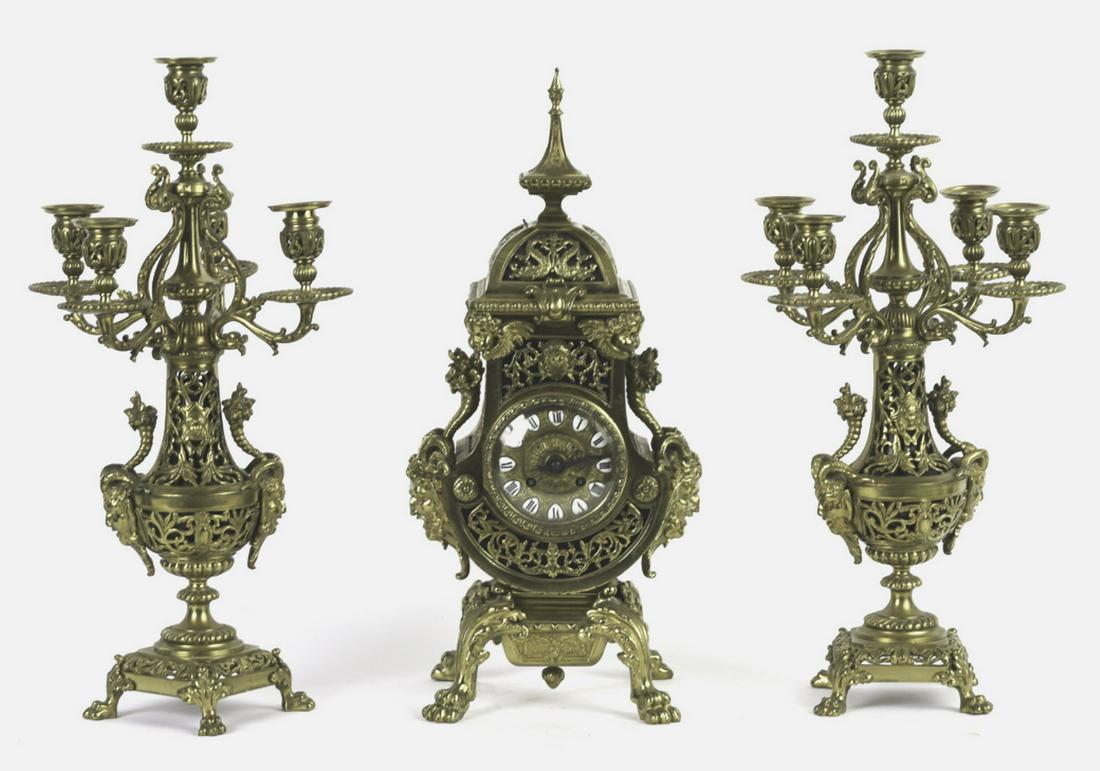 FRENCH RETICULATED BRASS GARNITURE SET: Including: (2) Five light candelabras and clock each mounted with Bacchus cast handles and cornucopia. 4 inch dial with chiming movement is unmarked.