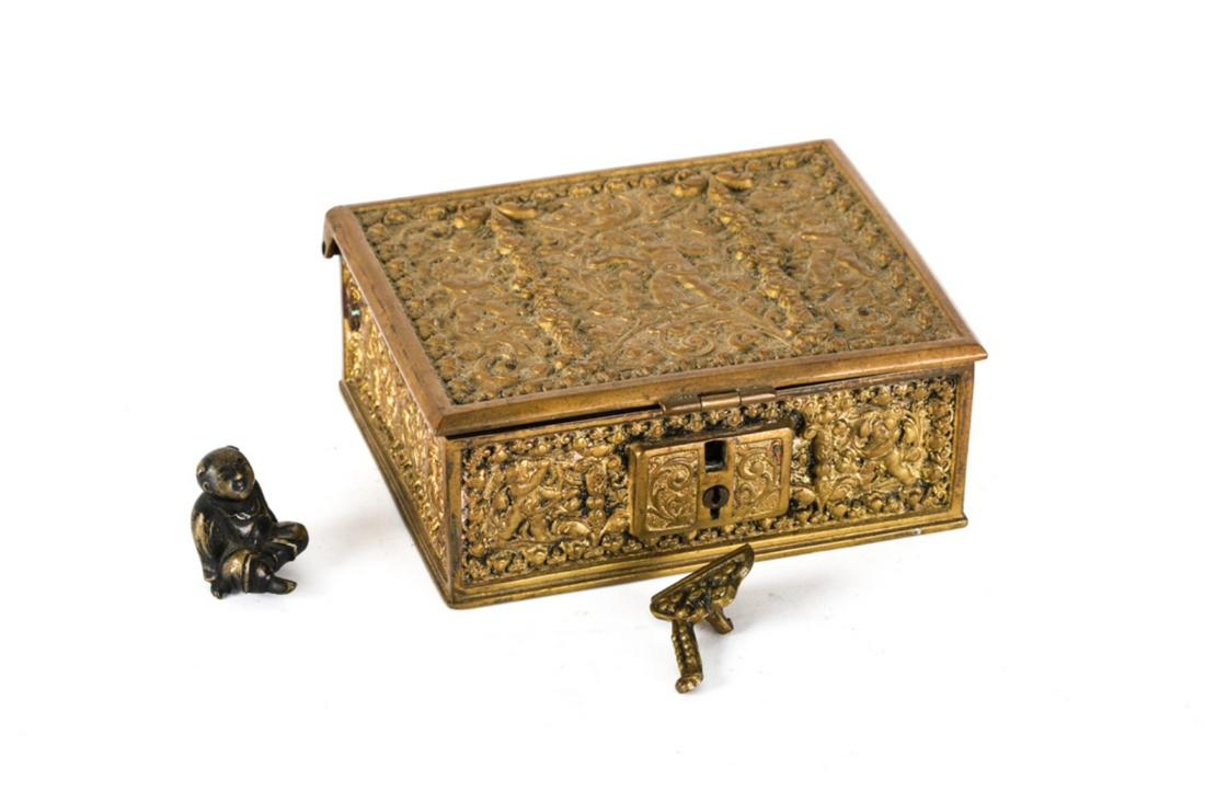BRONZE CONTINENTAL CIGARETTE BOX & CONTENTS: Cast in low relief with cherubs and scrolls. Locking hinged cover opens to wood lined interior containing bronze Buddha, mirror, bible etc. 2 x 5 x 4 inches.