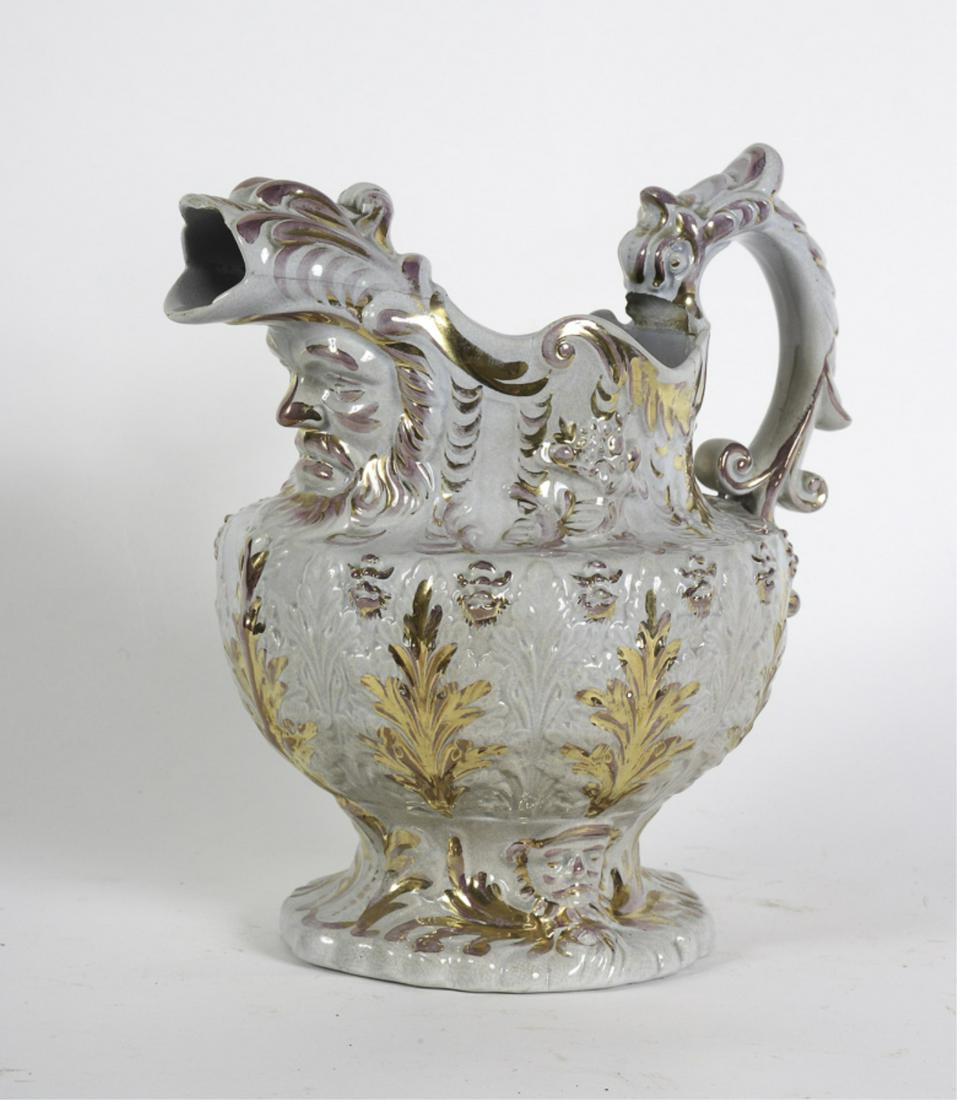 FIGURAL PINK & COPPER LUSTER PITCHER: Raised acanthus leaf ground with scrolled dolphin form handle and spout resting on Neptune's head. 10 inches Condition: Loss to handle, hairline from rim, chips to spout, Temp No 6384