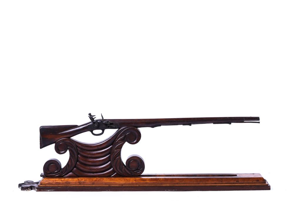 RARE MINIATURE BOSTON MILITIA CARVED FLINTLOCK: An early measuring device, miniature in form, flintlock musket with a metal flint lock and rod above an ornate bracket (all carved from a single piece of mahogany), slotted base which adjustably glide