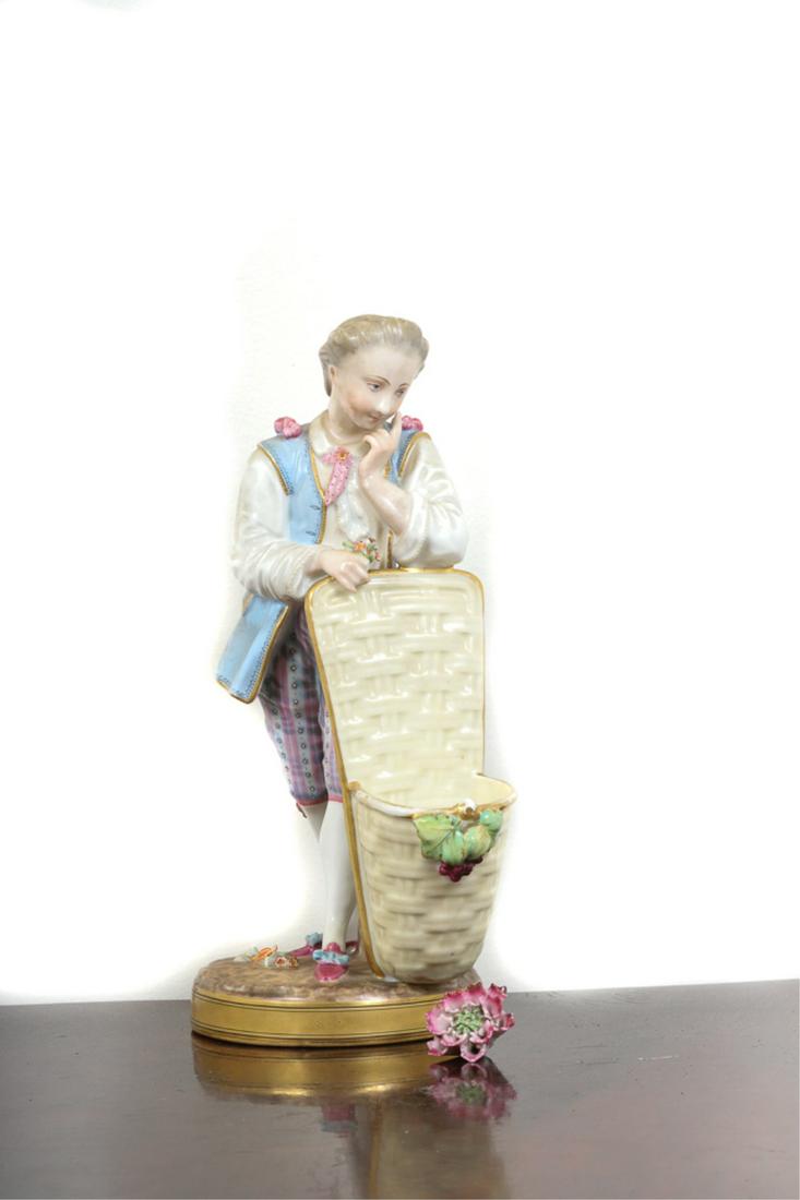 MEISSEN PORCELAIN FIGURINE: Young gentleman stands behind a basket for flowers. 10 1/2 inches. signed.