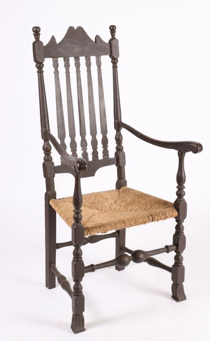 BANNISTER BACK SPANISH FOOT ARMCHAIR: Shaped crest, turned finials block and vase turnings, rush seat and Spanish feet, in old brown paint, black paint underneath. 48 x 24 x 21 inches
