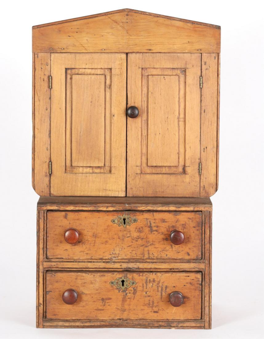 AMERICAN CLASSICAL PINE MINIATURE CUPBOARD: Greek revival crest with (2) molded doors that open to (4) shelves over a molded (2) drawer case with fancy brass escutcheons. 27 1/2 x 16 x 9 1/2 inches