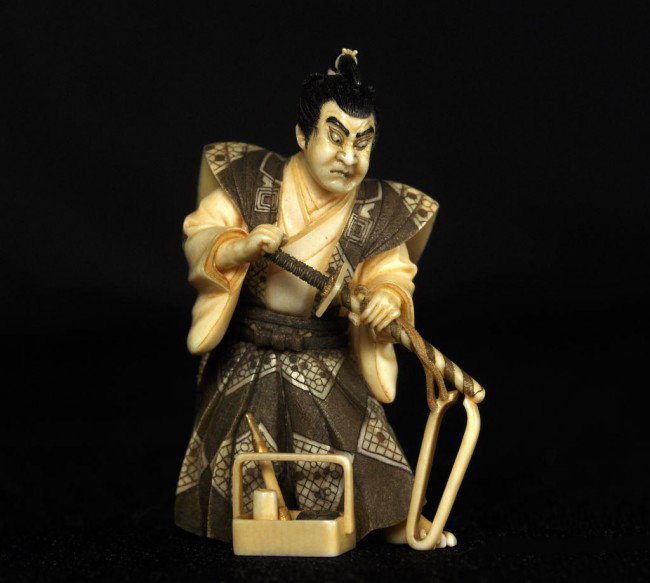 Japaneese Tinted ivory figural okimono, carved as : Japaneese Tinted ivory figural okimono, carved as a samurai warrior in formal dress and holding a sword, a smoking kit placed to the front, signed Masatoshi (possibly? Nakamura Tokisada, 1915-) Height