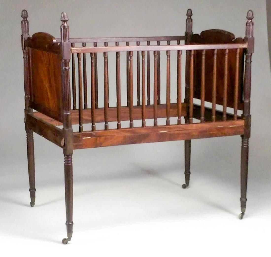 RARE ANTIQUE SHERATON CARVED MAHOGANY CHILD’S CRIB: 1st quarter 19th century, New York. In the manner of Duncan Phyfe. This high quality example with peaked head and foot boards, each with scrolled crest rail and joined to swelled fluted and ring-turne