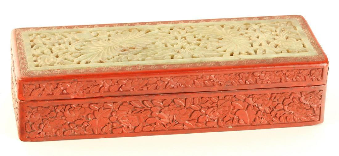 CINNEBAR BOX INLAID with WHITE JADE: Carved and pierced floral lid opens to a divided interior 2 1/2 x 10 1/2 x 3 3/4 inches Condition: Jade has a diagonal crack right of center Temp No 6071