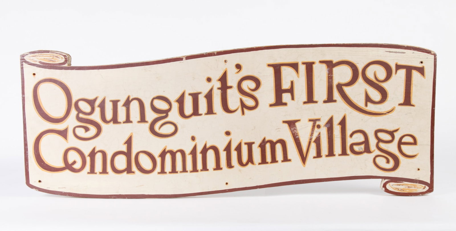 PAINTED WOOD SIGN: "OGUNQUIT'S FIRST CONDOMINIUM: VILLAGE". Scroll-shaped wood sign with hand-painted lettering brown letters with gold trim. 11 x 30 inches.