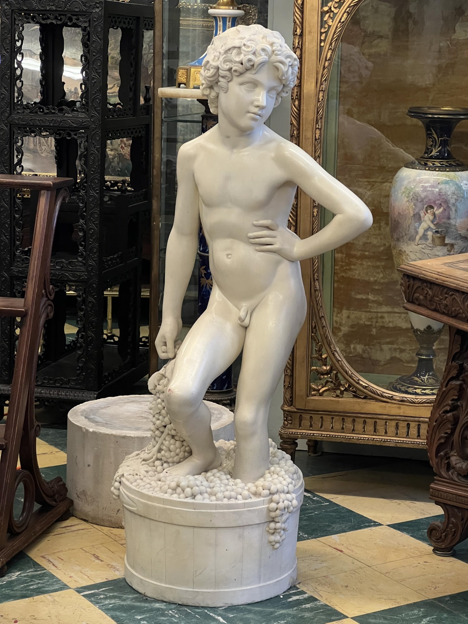 THE WINE MAKER - CARVED ITALIAN CARRARA MARBLE: (19th c) carved Italian Carrara marble figure of a Bacchanalian youth crushing grapes in a barrel. 50 inch height. Condition: Good, painted over with a white glaze. Temp No 3017