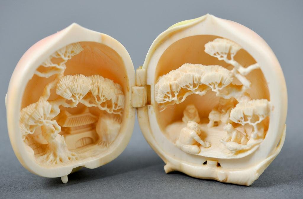 Asian Signed Carved Ivory Box: Very finely carved figural fruit shaped box tinted pale peach with green leaves opens to reveal figures and animals in a Chinese landscape signed in characters on stem Condition: good Size: 2"good2"
