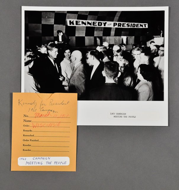 1960-Mar 10, J.F.K., "Meeting the People": (1) Photograph with negative of J.F.K. in Wisconsin on March 10, 1960, 8" x 10". Together with Kennedy '60 pin. Condition: Good