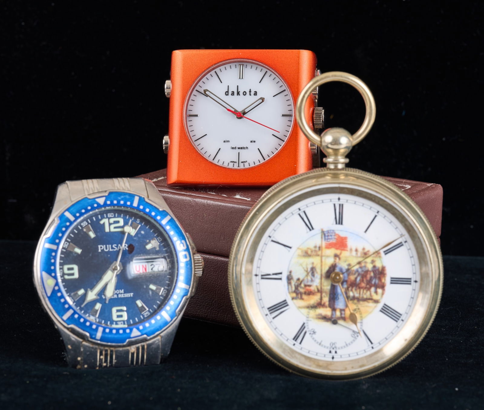 MODERN DESK, WRIST, & POCKET WATCHES: Pulsar wrist watch, Dakota desk clock, & pocket watch with Civil War scene. Wrist watch measures 5 inches. Condition: Untested. Temp No 2965