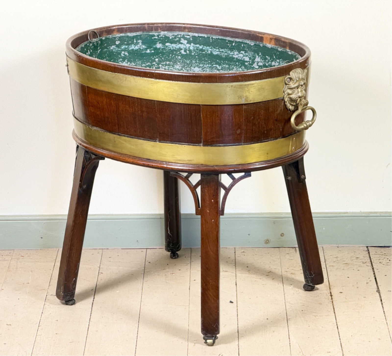 GEORGE III BRASS BOUND MAHOGANY CELLARETTE: Oval cellarette with lions head handles and zinc lining atop (4) Marlborough legs with pierced adornment. 24 x 25 x 17 1/2 inches.