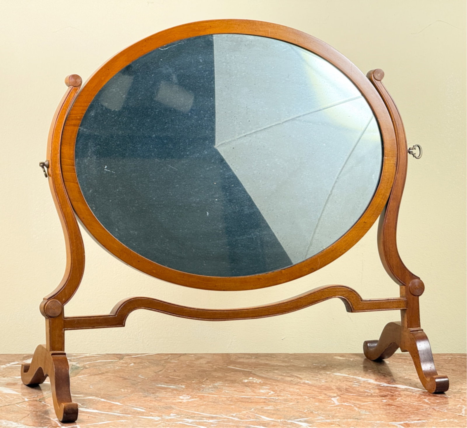 REGENCY SATIN WOOD SHAVING MIRROR: Oval mirror with carved decoration on scrolled feet. 19 1/2 x 21 inches.