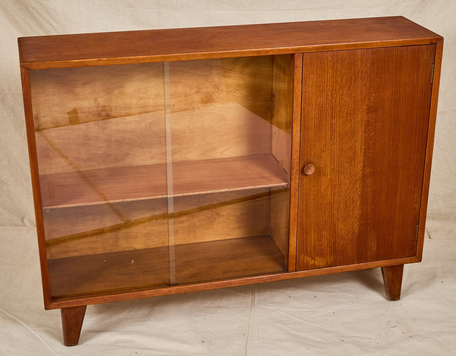 LEBUS TEAK WOOD BOOKCASE with SLIDING GLASS DOORS: Lebus Furniture mid century teak bookcase with sliding glass doors and a single door cabinet, raised on flared tapered legs. Label inside door. 31 1/4 x 42 x 10 inches.