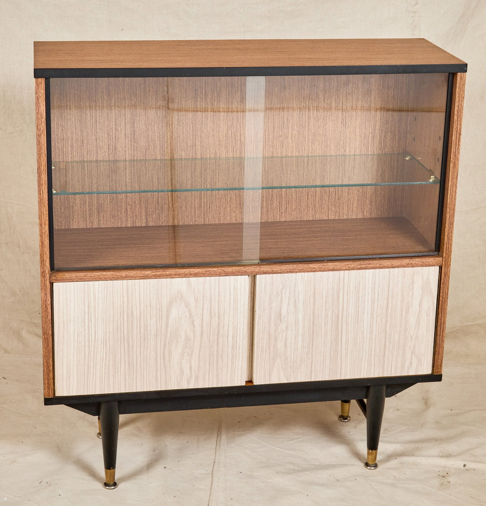 BERRY MID-CENTURY CABINET with SLIDING GLASS DOORS: Finished with two-tone veneer and black trim accents, (2) sliding glass doors with shelf and a lower (2) door cabinet. 39 x 26 x 11 1/2 inches.