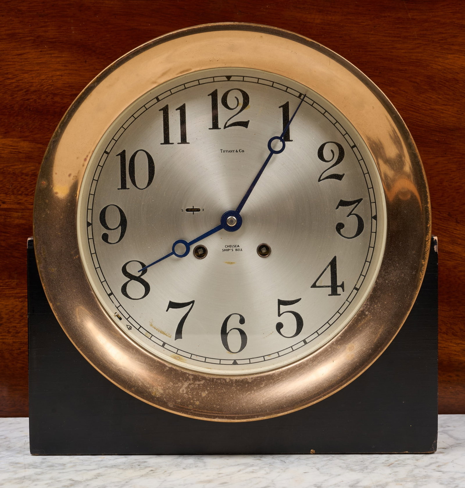 TIFFANY & CO CHELSEA SHIPS BELL PRESENTATION CLOCK: 10 inch brass case presented to "John E. Shepherd 'The Great One' from his friends and associates November 24, 1987" on custom wooden base, 7 1/2 inch engraved silver dial with Breguet hands & Tiffany