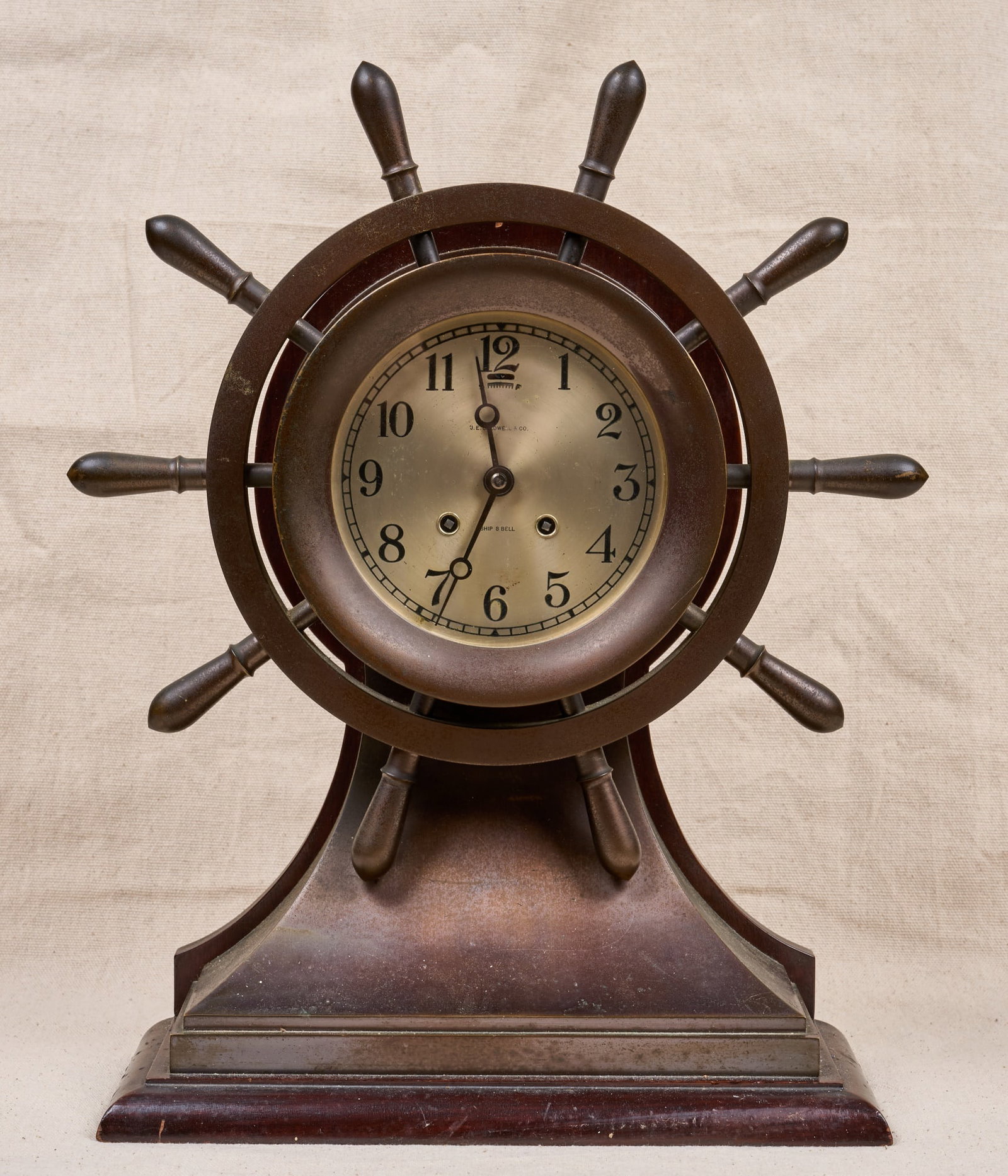 J.E. CALDWELL & SON CHELSEA SHIPS BELL CLOCK: Bronze ship wheel form case with wooden base, 5 1/4 inch engraved silver dial with J.E. Caldwell & Co. (Philadelphia) retailers mark, ships bell chime. 17 1/2 x 12 1/2 x 5 1/2 inches.