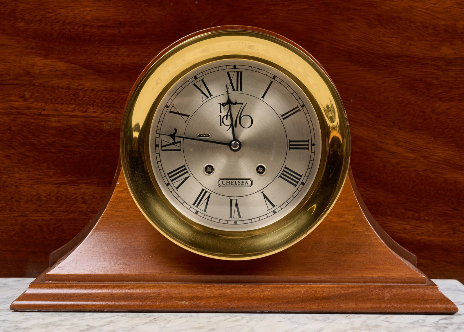 CHELSEA CLOCK CO. BICENTENNIAL MANTEL CLOCK: 7 1/4 inch brass case, 5 1/4 inch engraved silver case with 1776/1976 insignia, wooden base. Limited Edition no. 008. 9 1/4 x 14 x 4 inches.