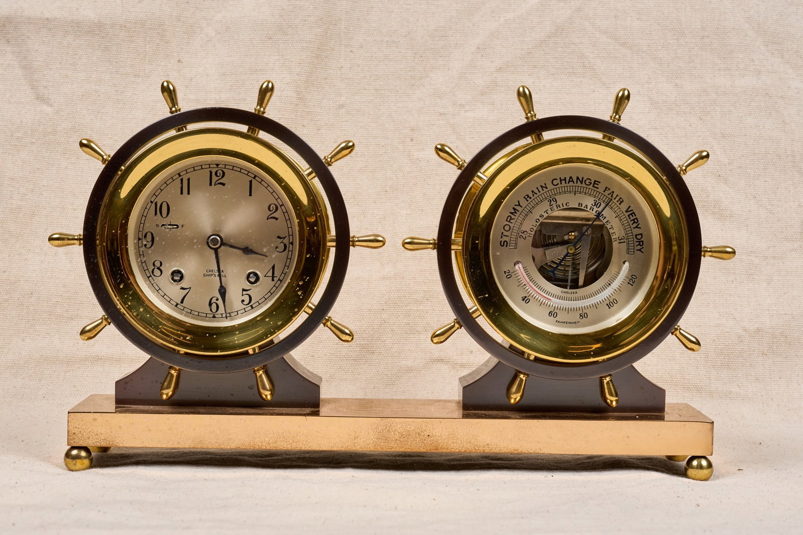 CHELSEA BRASS SHIPS BELL CLOCK BAROMETER: 4 3/4 inch brass & bronze ships wheel form cases, 3 1/2 inch engraved silver dial. 9 x 14 x 3 inches.