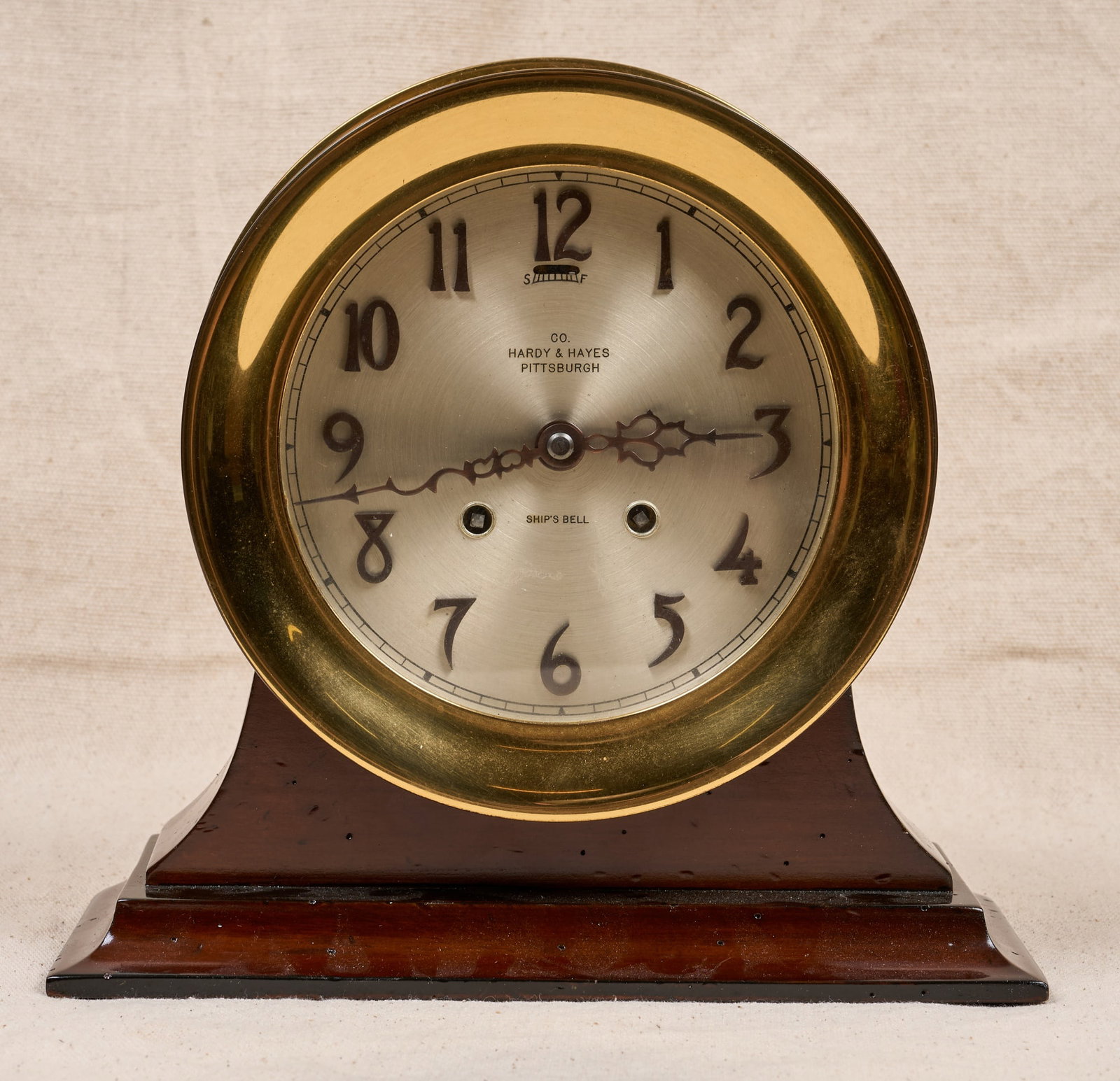 HARDY & HAYES CO. CHELSEA SHIPS BELL CLOCK: 7 1/4 inch brass case, 5 1/4 inch silver dial with bronze numerals, fancy hands and Hardy & Hayes Co. (Pittsburgh) retailers mark , custom wooden base. 9 x 9 1/2 x 4 inches.
