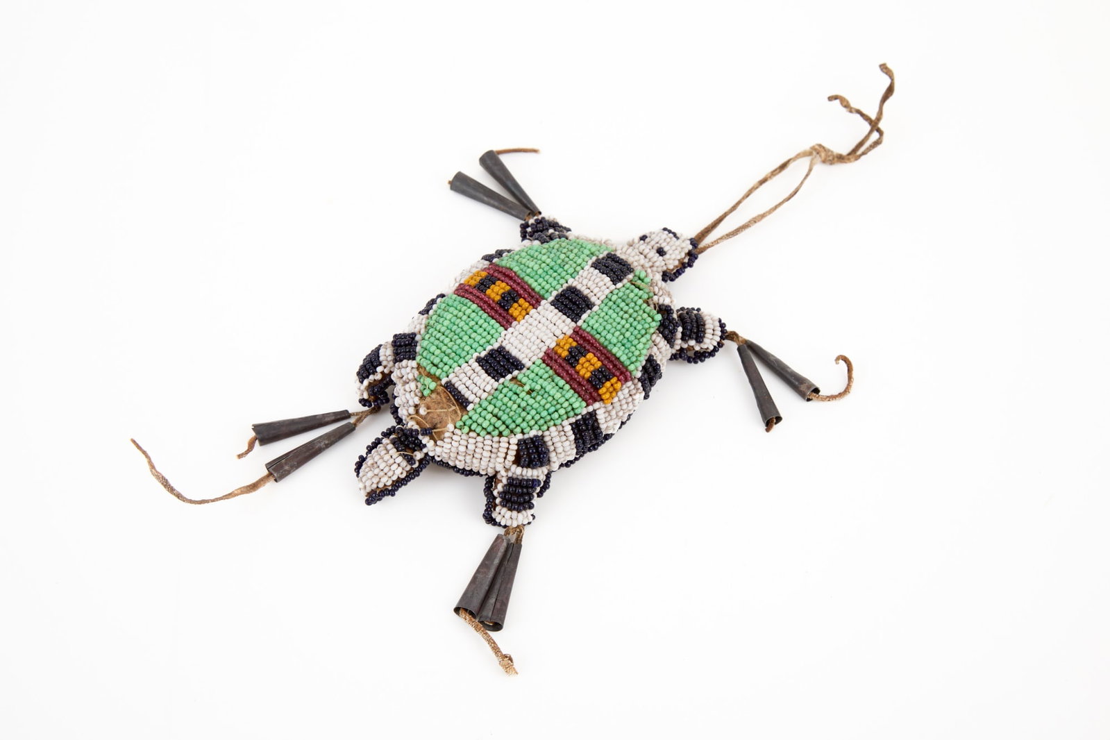 PLAINS INDIANS BEADWORK UMBILICAL TURTLE FETISH: Tanned hide turtle form umbilical fetish with geometric polychrome beadwork & tin cone tassels. 4 1/2 x 2 1/2 inches.