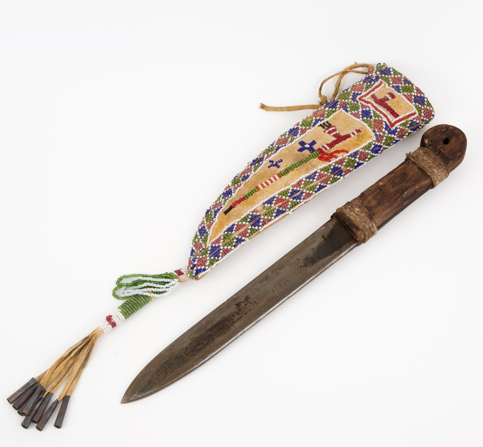 PLAINS INDIANS KNIFE with BEADWORK SHEATH: Knife with primitive wooden handle carved with recess for inlay, rawhide sheath with geometric polychrome beadwork border surrounding beadwork images of catlinite peace pipes, beadwork & tin cone tass