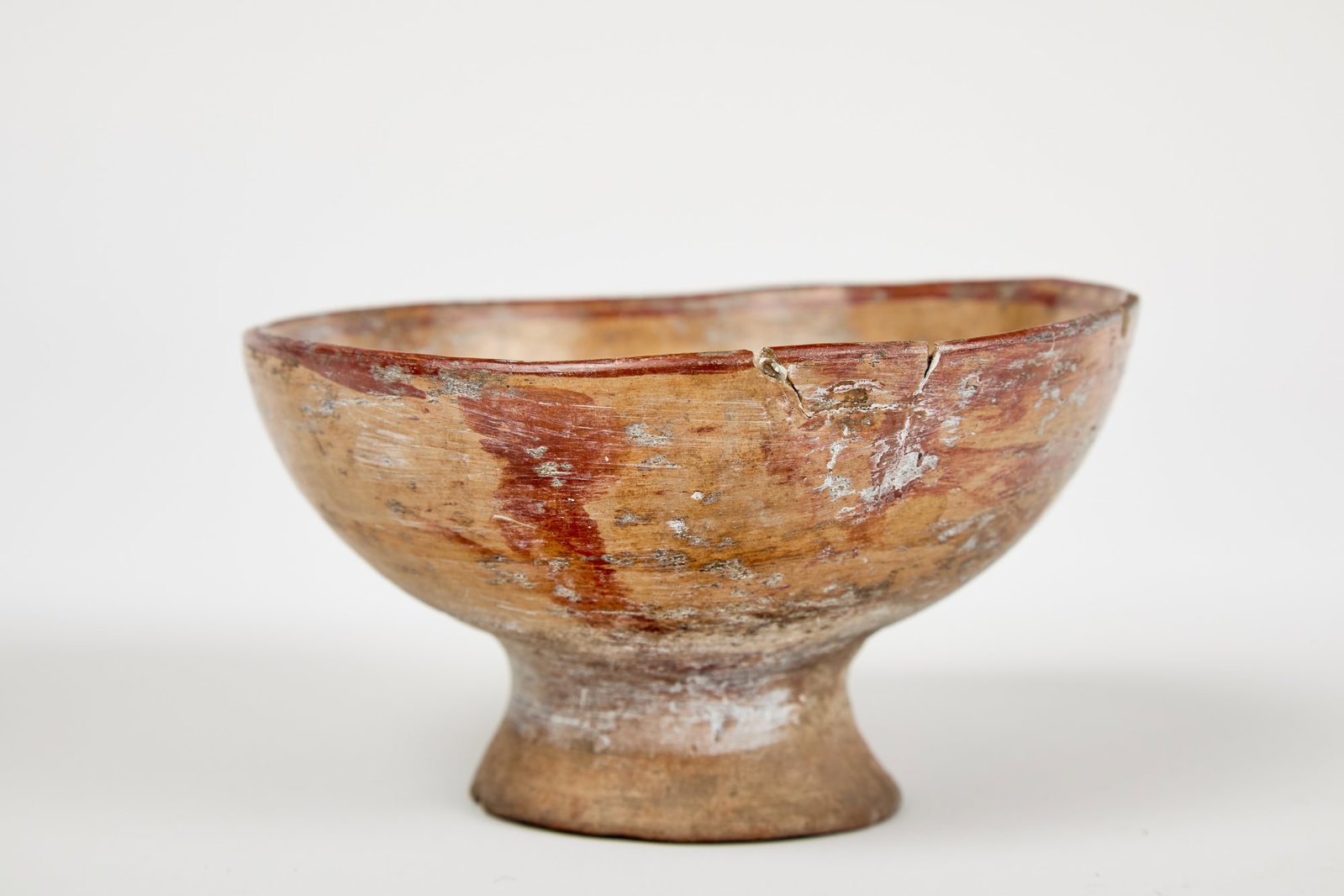 PAINTED PRE-COLUMBIAN FOOTED EARTHENWARE BOWL: Pre-Columbian footed earthenware bowl with red double stripe around rim and geometric design in basin, possibly a depiction of the sun. 3 1/2 x 6 inches.