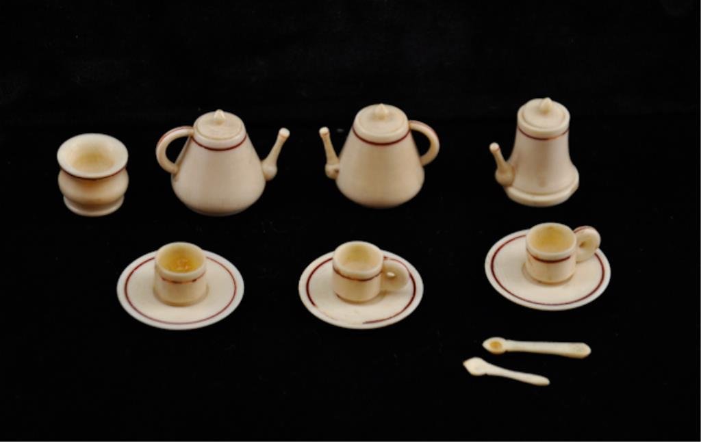 Miniature Ivory Tea Set: Consisting of (3) pots, a sugar bowl, (3) cups and saucers and (2) spoons in a small round wooden box. Tallest pot measures 1 inch. Condition: Good with two handles unglued